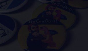 Multiple buttons on a table with a person and a baby on them that says 'He Can Do It!'