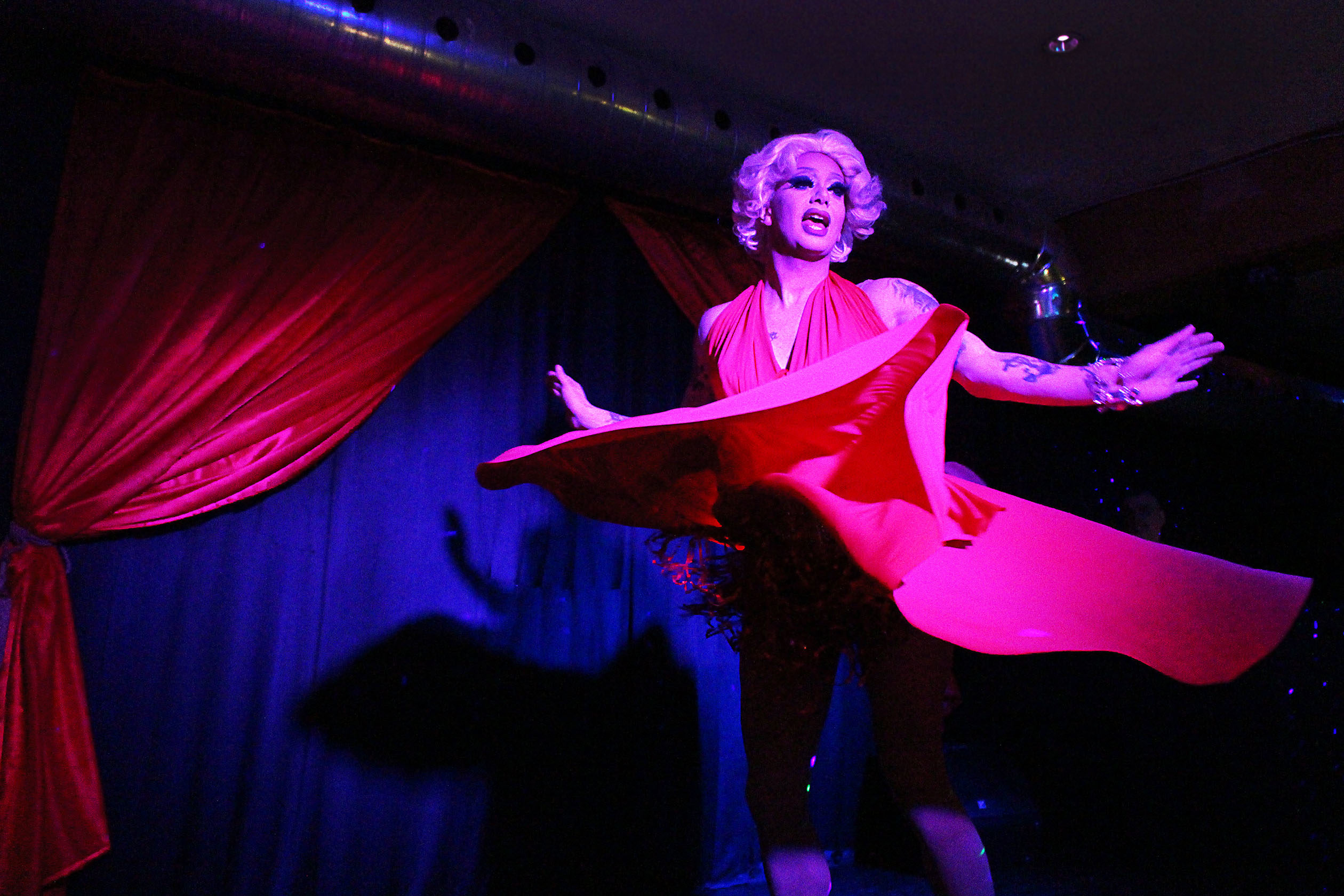 Scarlett Bobo performing on stage in a red outfit, with red curtains in the background.