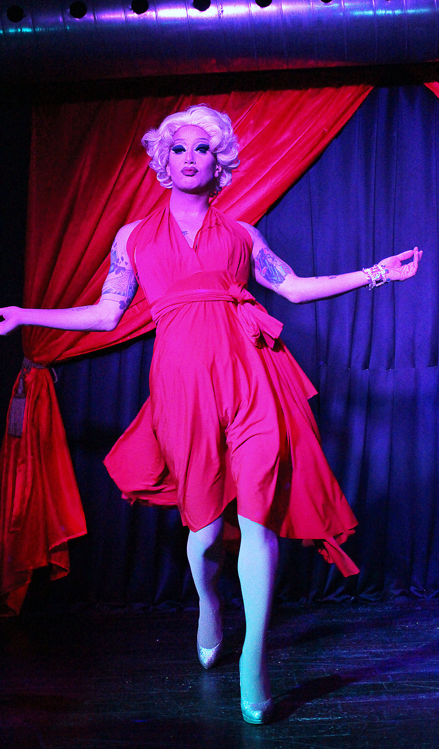 Scarlett Bobo on stage in a red outfit, with red curtains in the background.