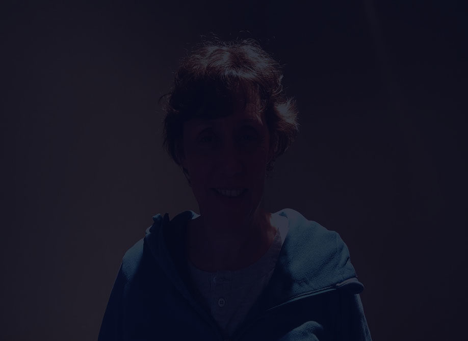A photo of Bonnie Flatt, wearing an aqua-coloured sweater, looking at the camera. There is a dark overlay over the image.
