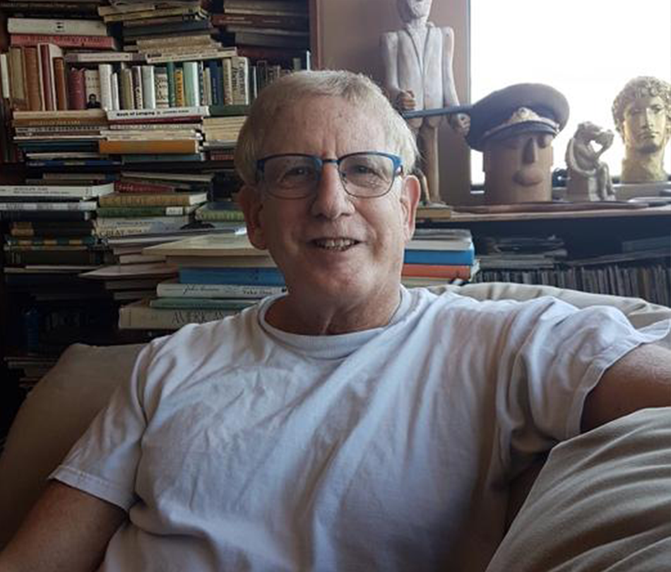 A photo of a person in a white shirt, sitting on a couch smiling with books in the background.